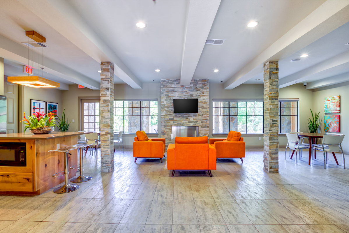 Community clubhouse with lounge, kitchen to the left, beautiful nature views, wood-style flooring, couch, dining area to the right, and bar seating.