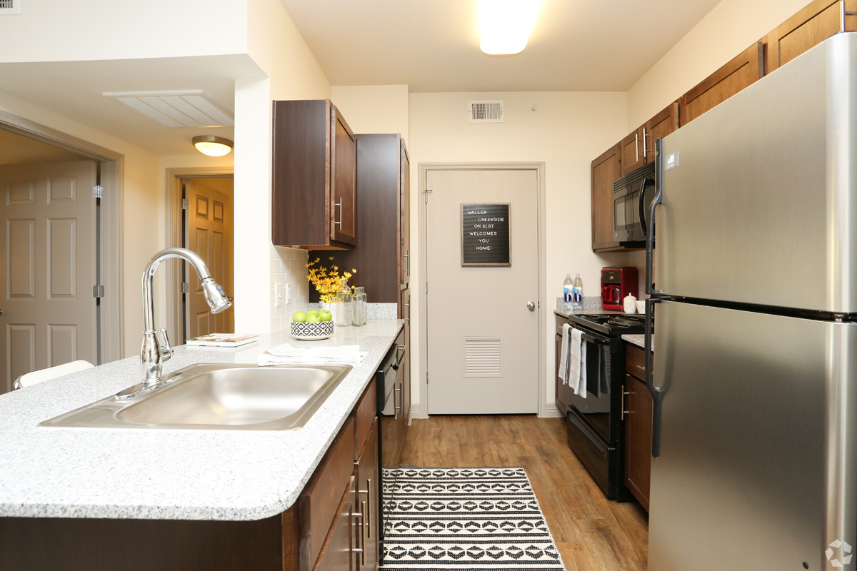 Model kitchen with stainless steel fridge, black microwave and stove, wood-style floors and granite countertops